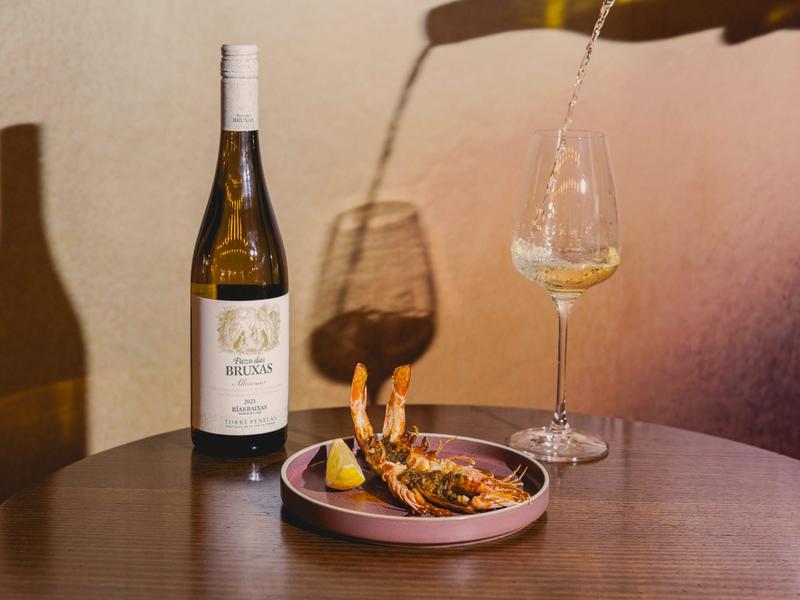 Bottle of Pazo das Bruxas Albariño wine with grilled prawns and a glass being poured, photographed at OLÉ Restaurant, South Bank.