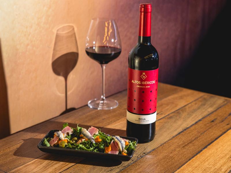 Bottle of Altos Ibéricos Crianza 2020 Rioja red wine with a glass and anchovy salad, photographed at OLÉ Restaurant, South Bank.