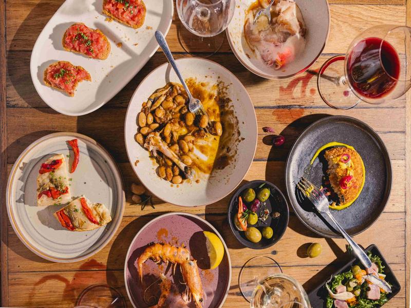 Overhead shot of a Spanish tapas feast including prawns, olives, beans, croqueta, and red wine at OLÉ Restaurant.