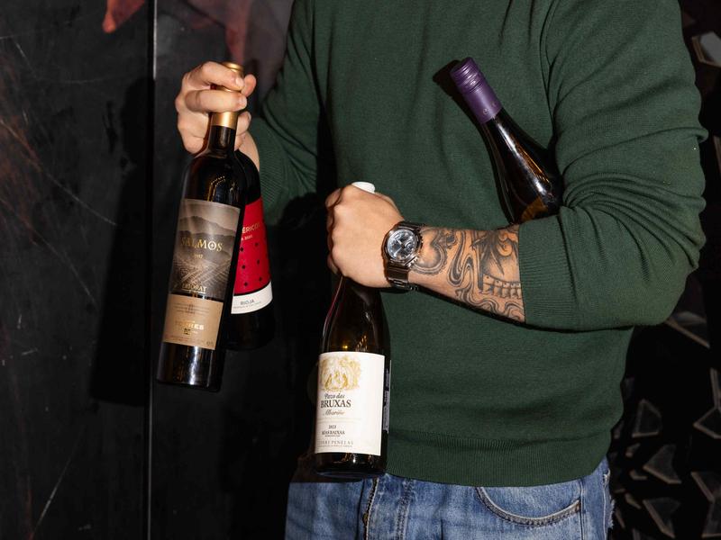 Tattooed staff member holding bottles of Familia Torres wines including Salmos, Altos Ibéricos, and Pazo das Bruxas at OLÉ Restaurant.